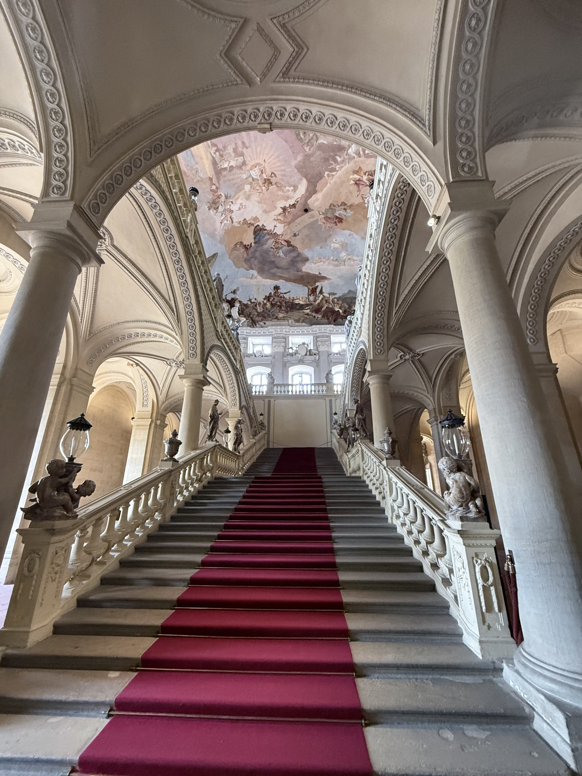 Gebäudereinigung Treppenaufgang der Würzburger Residenz mit rotem Teppich und Malerei an der Decke